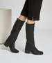 Black knee-high leather boots with a side zipper, a slightly rounded square toe, and a low block heel, worn with black pants. 3