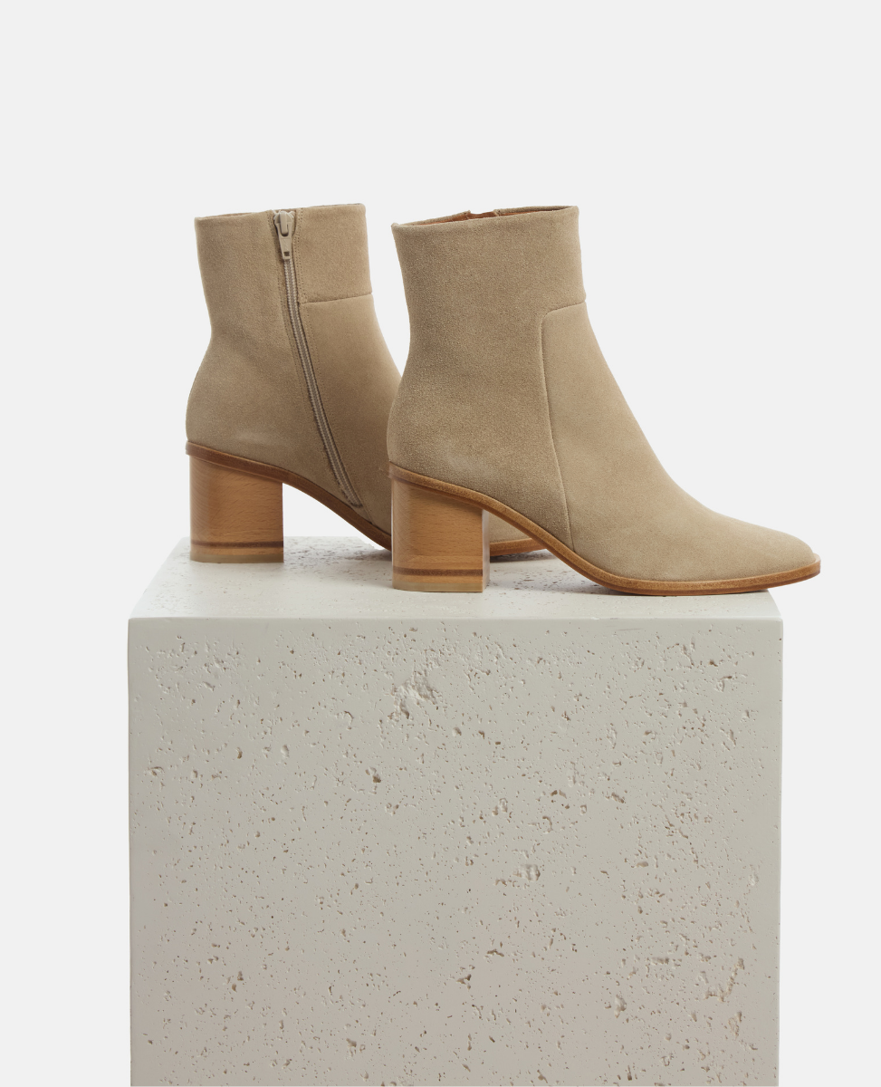 Pair of beige ankle boots on a light gray pedestal with a white background