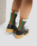 Person wearing brown platform shoes with green and brown patterned socks on a light background 3