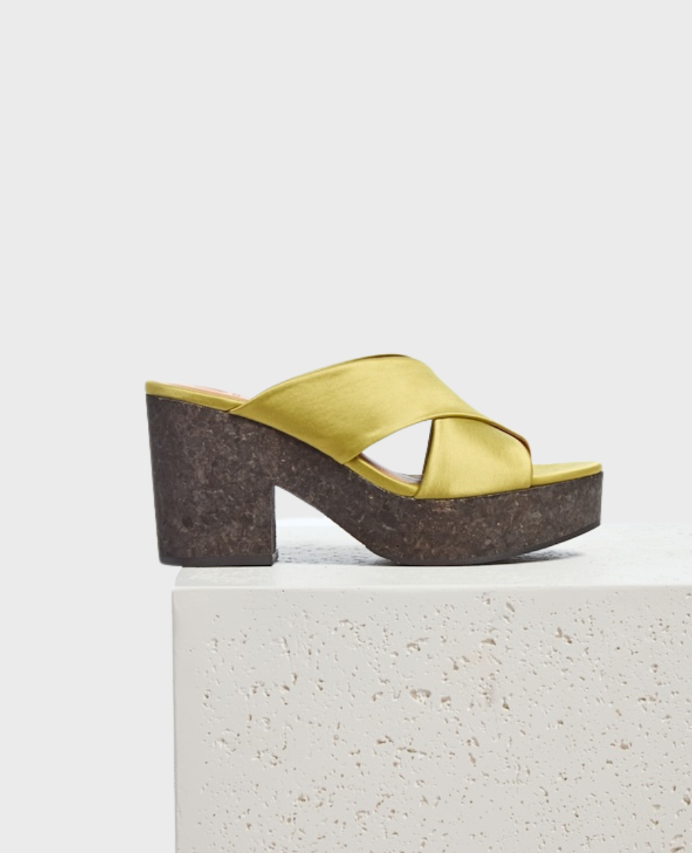 A stylish sandal featuring a mustard yellow satin crisscross strap design, a chunky cork platform heel, and a smooth, open-toe silhouette.
