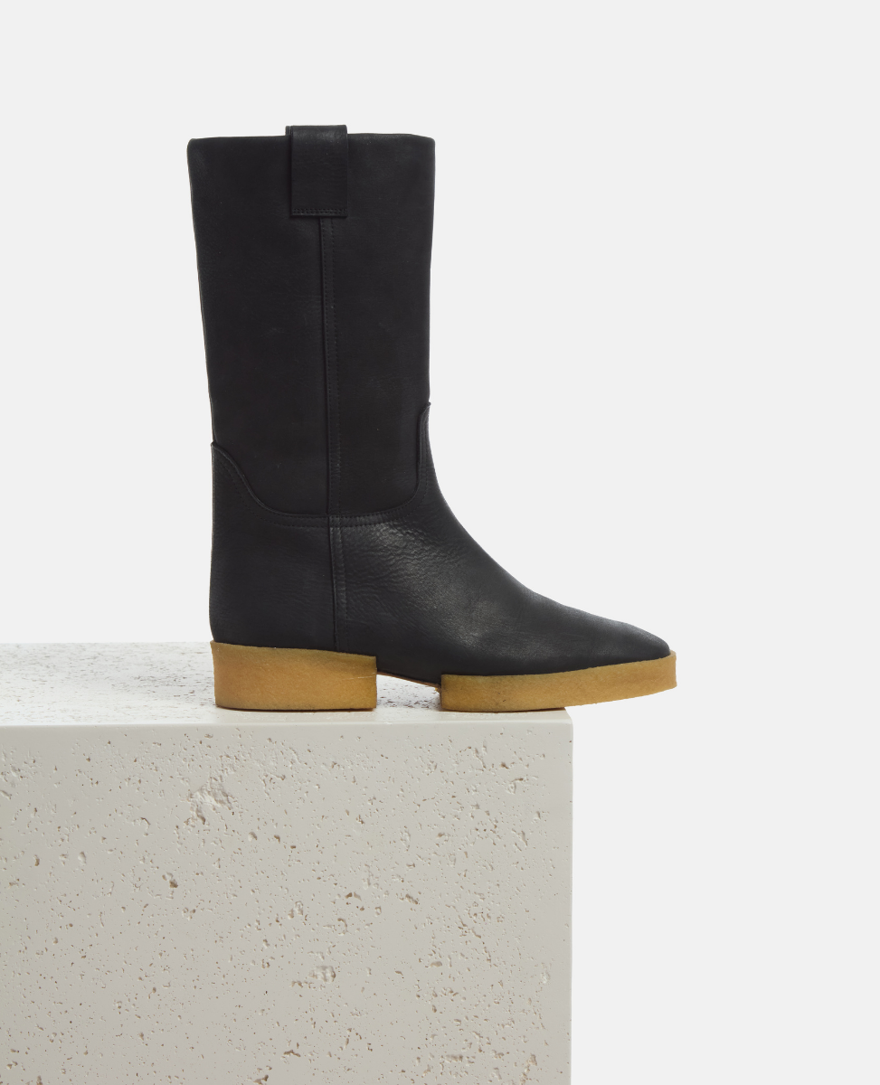 Black knee-high boot with brown sole on a light gray background