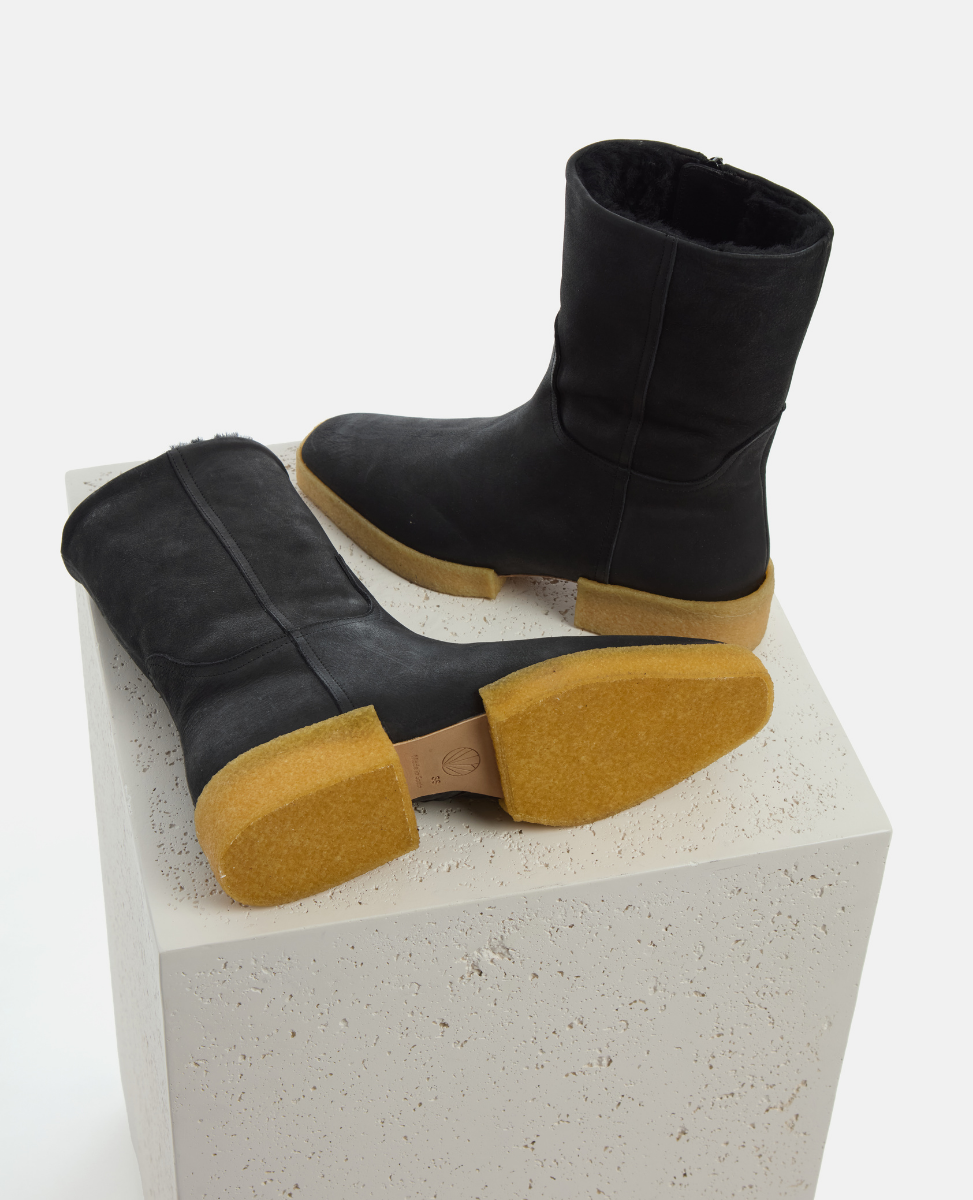 Black boots with yellow soles on a white pedestal
