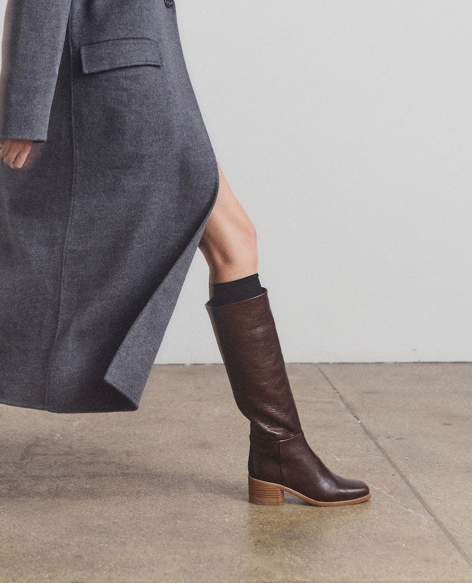 Brown knee-high boots worn with a gray coat on a neutral background