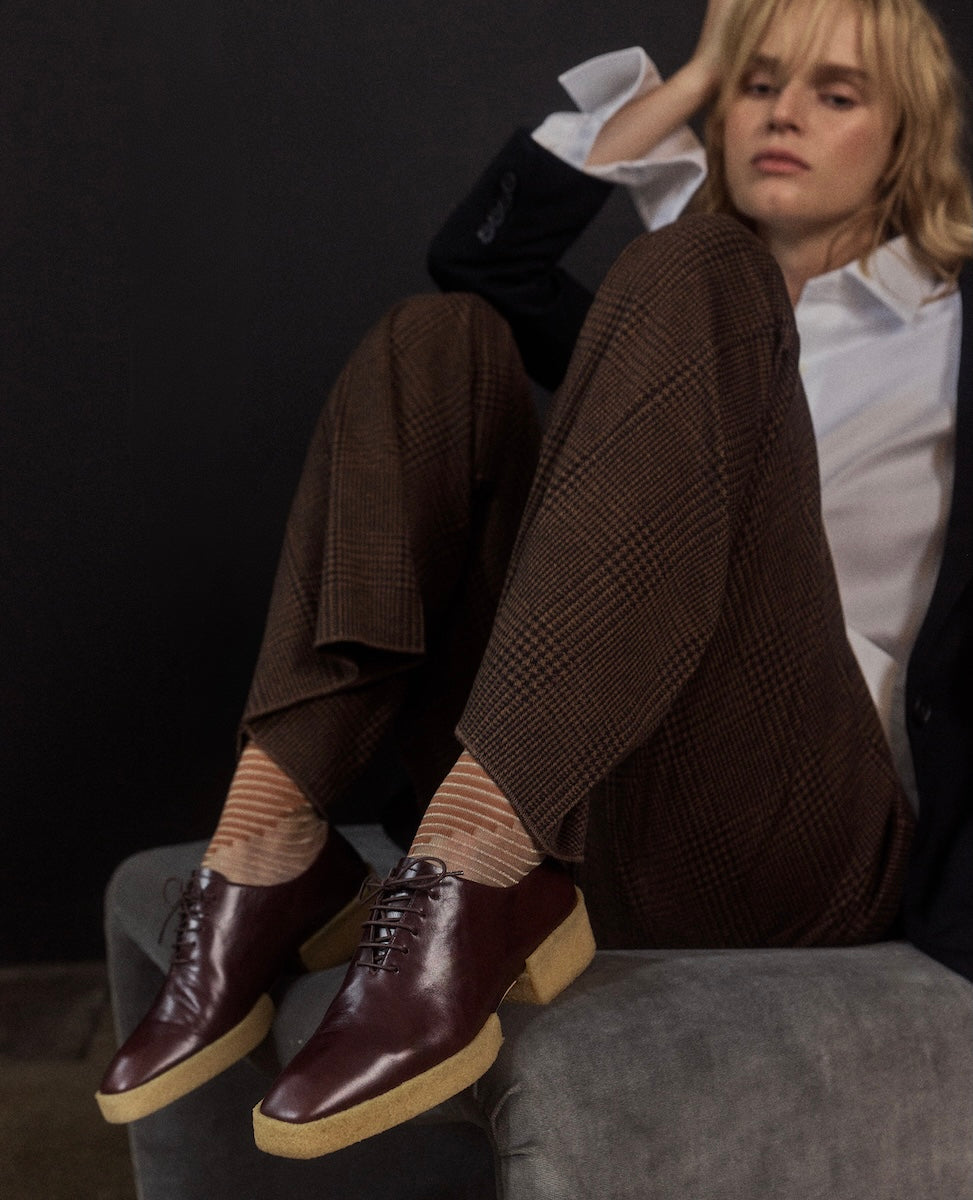 Person wearing tweed pants with oxblood leather crepe sole oxfords sitting on a chair