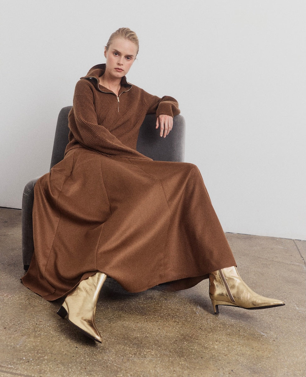 Woman wearing a brown dress and gold boots sitting on a chair.