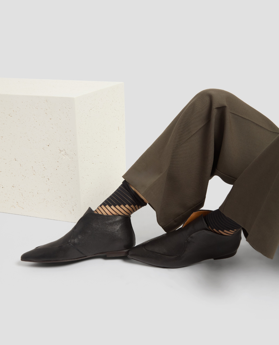 Person wearing black shoes and brown pants sitting on a white surface with a textured white cushion.