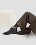 Person wearing black shoes and brown pants sitting on a white surface with a textured white cushion. 5