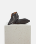 Pair of black pointed-toe shoes on a light gray pedestal against a white background 1