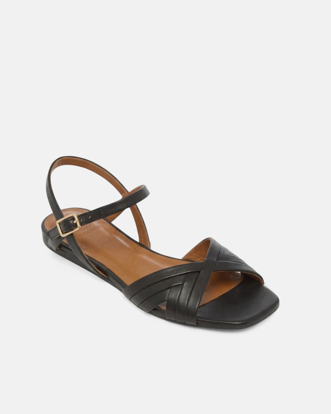 Angled view of a black leather flat sandal with slim crisscross toe straps, buckle quarter strap, and square toe, on a pale grey background.