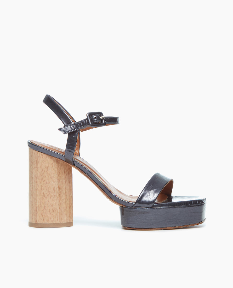Side view of Angel platform sandal makes a statement in black pearl patent leather featuring a single strap across the toes is paired with a clean quarter strap and a covered buckle.