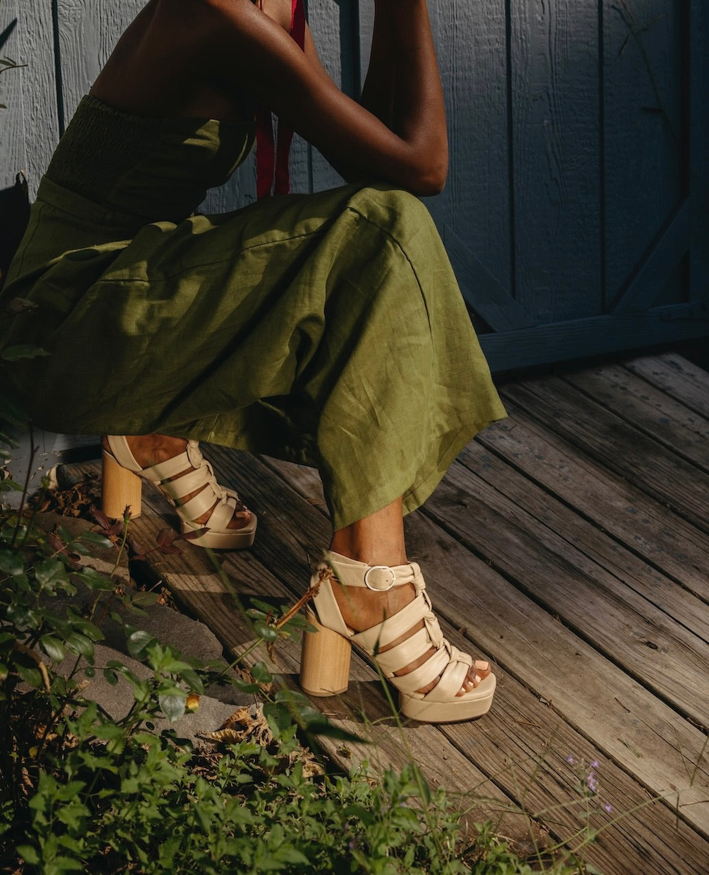 Woman crouched down outside wearing a green jumpsuit and the April Heel in Latte Machiatto.