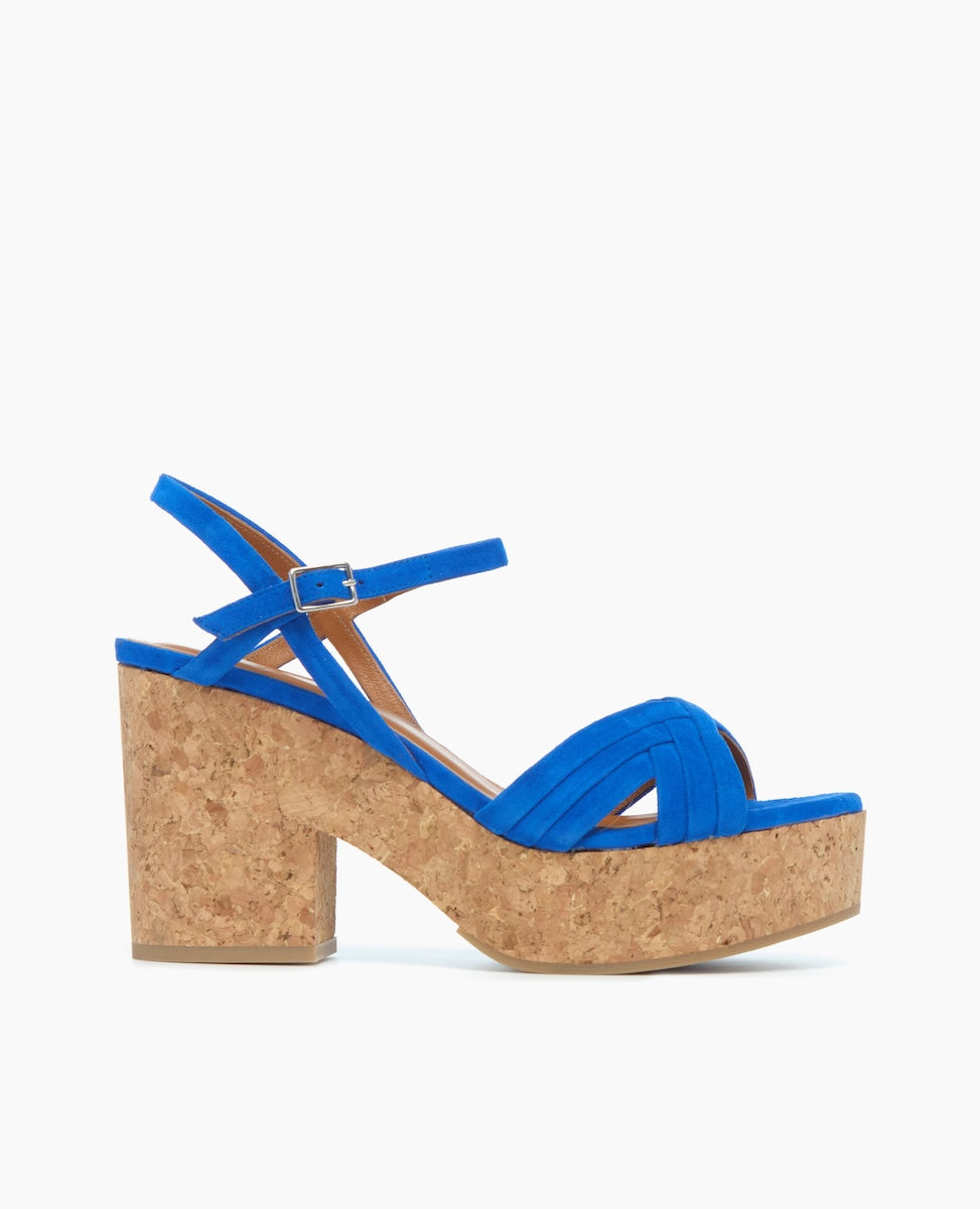 A vibrant blue sandal with a suede-like texture features a thick cork platform heel, an open toe design with crisscross straps, and an adjustable ankle strap with a small buckle.