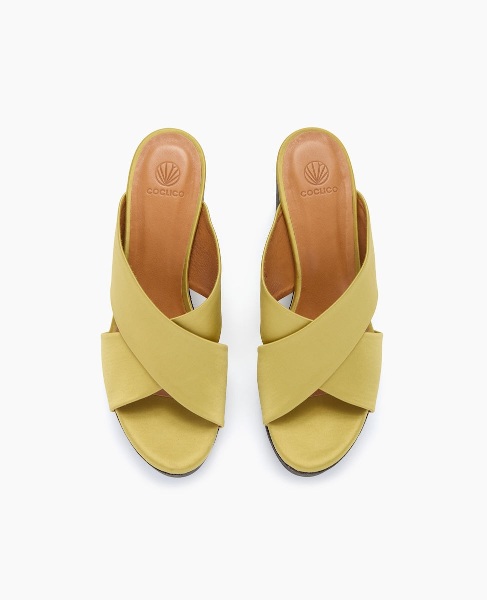 These sandals feature a mustard yellow color with wide, crisscrossing leather straps, an open toe design, a tan insole with branding, and a low, flat sole.
