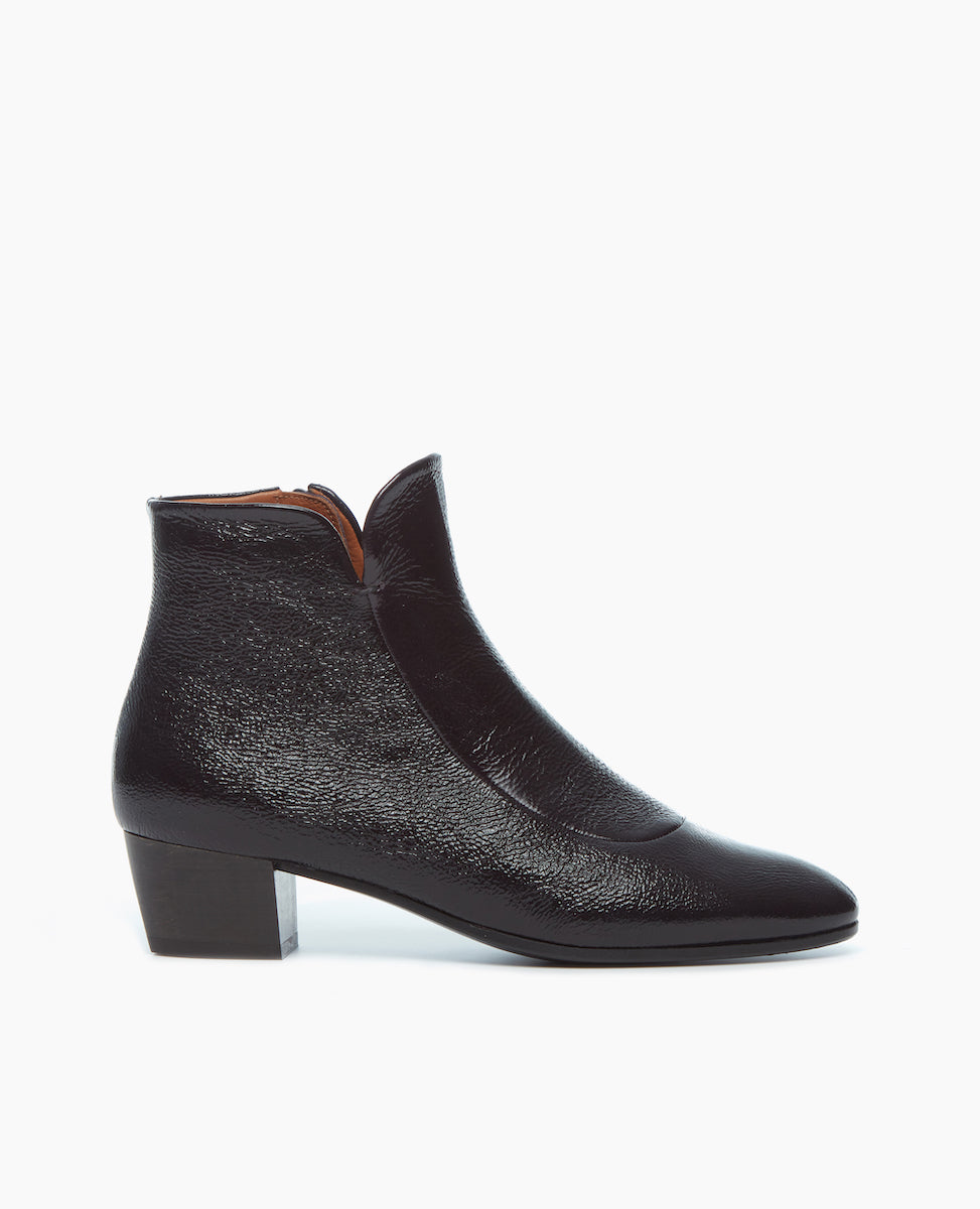 Side view of Coclico Calm Boot in amethyst patent: classic black leather grounded by a solid wood angled heel, featuring a bid front insert and an almond toe shape. 