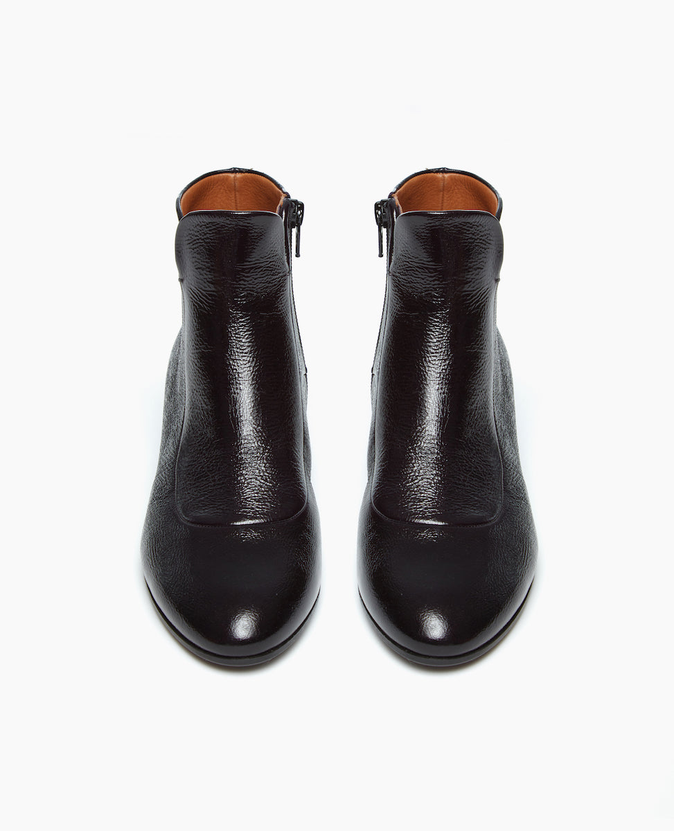 Coclico Calm Boot in amethyst patent displayed from the front: classic black leather grounded by a solid wood angled heel, featuring a bid front insert and an almond toe shape. 