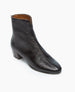 A sleek, black, mid-ankle boot with a glossy, textured leather finish, an almond shaped toe, a back zipper, and a low, block heel. 6