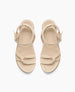 Beige sandals with a smooth texture feature two knotted straps across the toes, an adjustable ankle strap with a silver buckle, and a flat sole. 4