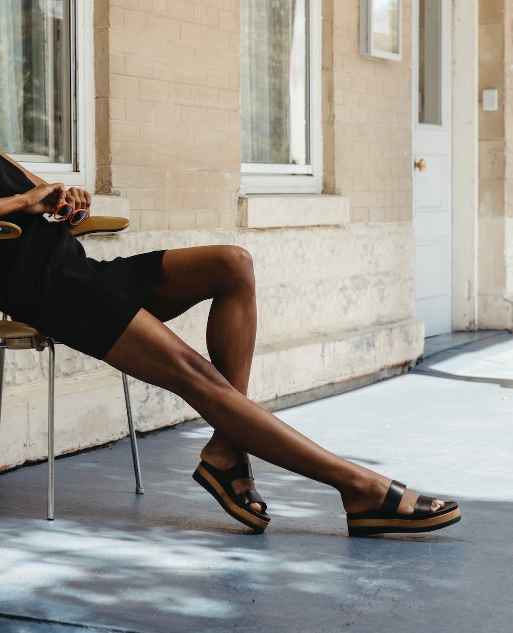 Legs stretched out against concrete with the left leg bent wearing the Dana Wedge in Black. 