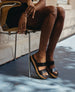 Legs of a woman sitting on a wooden chair with her arms leaned over the legs and the toes pointed down.  2