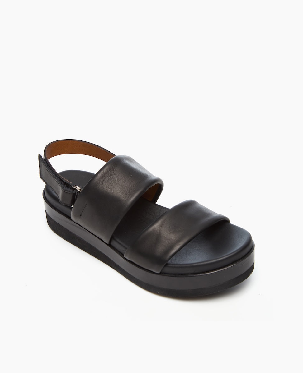 A black leather sandal with a thick platform sole, featuring two wide straps across the foot and an adjustable ankle strap with a buckle.