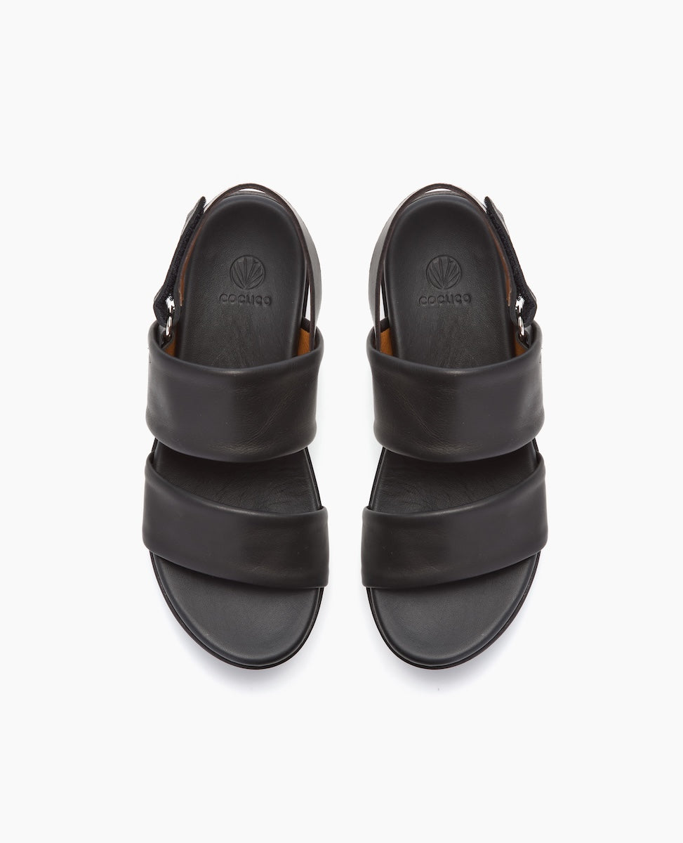 A pair of black leather sandals with two wide straps across the top, a closed heel, and a round toe, featuring a subtle embossed logo on the insole.