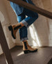 Tan suede ankle boots with black elastic side panels, a chunky black heel, and a rounded toe, worn with rolled-up blue jeans. 3