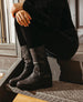 Black, mid-calf leather boots with a smooth texture, round toes, and low block heels, worn by a person dressed in black clothing, seated on a metal staircase. 6