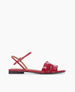 A sleek red sandal with a glossy finish features a flat sole, an open toe design, a thin ankle strap with a buckle, and a distinctive cut-out pattern on the front strap. 3