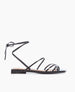 A sleek black sandal featuring thin, glossy straps that wrap around the ankle, a flat sole, and a minimalist design with a knot detail at the back. 2