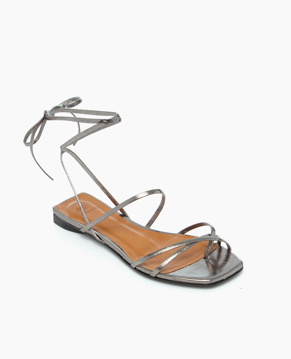A sleek, metallic silver sandal with a square toe, thin straps, and an ankle tie, featuring a flat sole and a smooth, glossy finish.