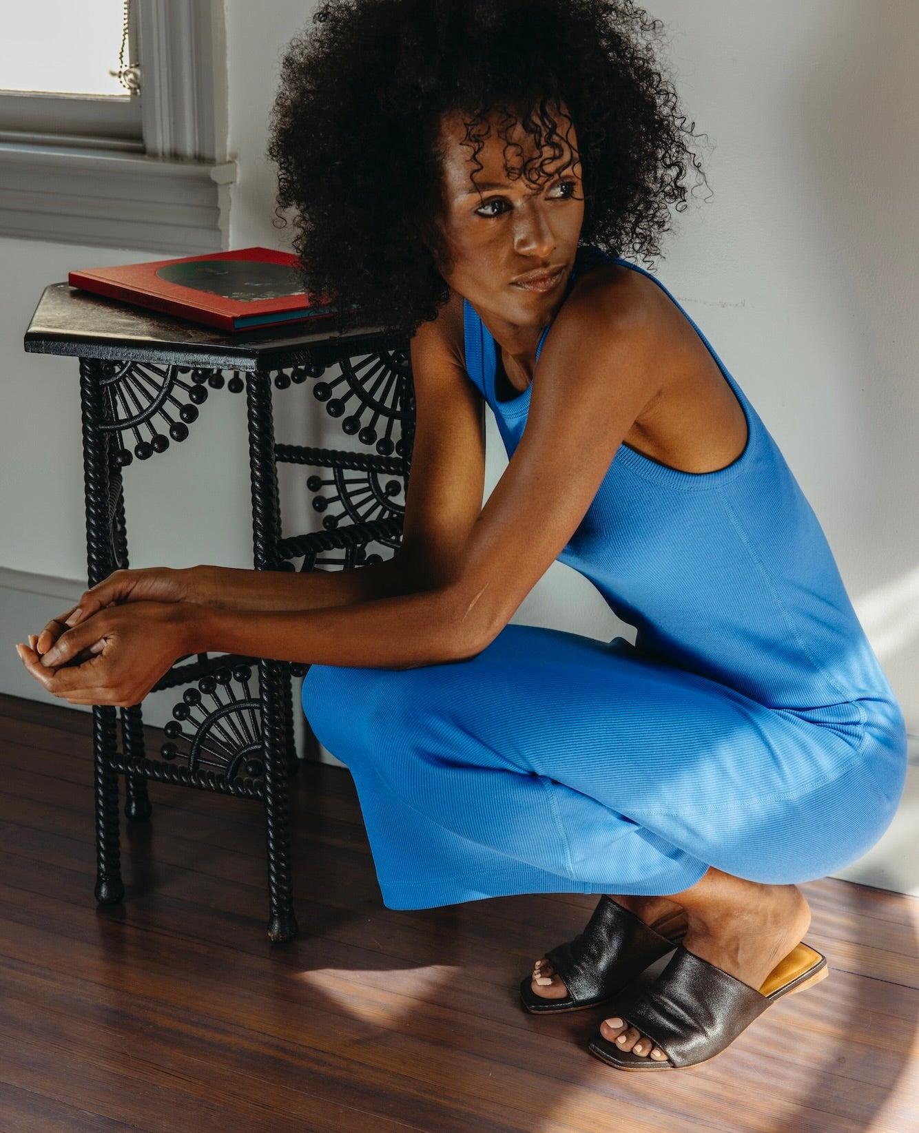 Woman wearing a blue dress bent down wearing the Ferhana Sandal in anthracite shimmer suede.