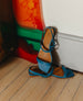 The Fifi Sandal in Cerulean leather with the right pair propped up against the wall placed on top of the left pair.  2
