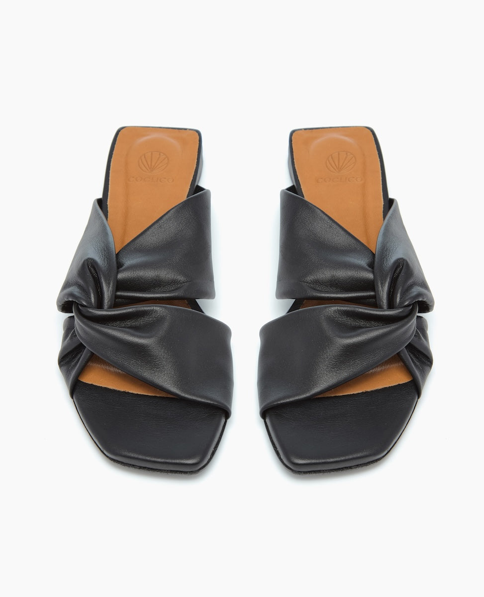 Black leather sandals with a twisted strap design, featuring a square open toe and a tan insole.