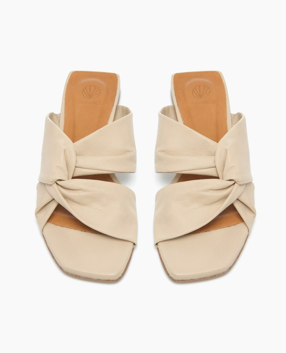 Beige slip-on sandals with a knotted design feature wide straps, a square open toe, and a tan insole, crafted from smooth leather.