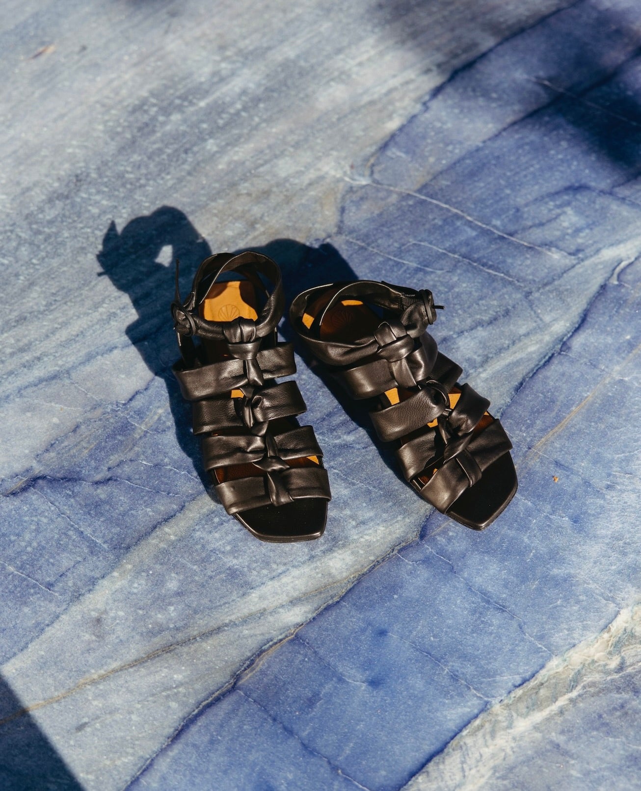 Pair of the Flair Sandal in Black placed on blue marble flooring.