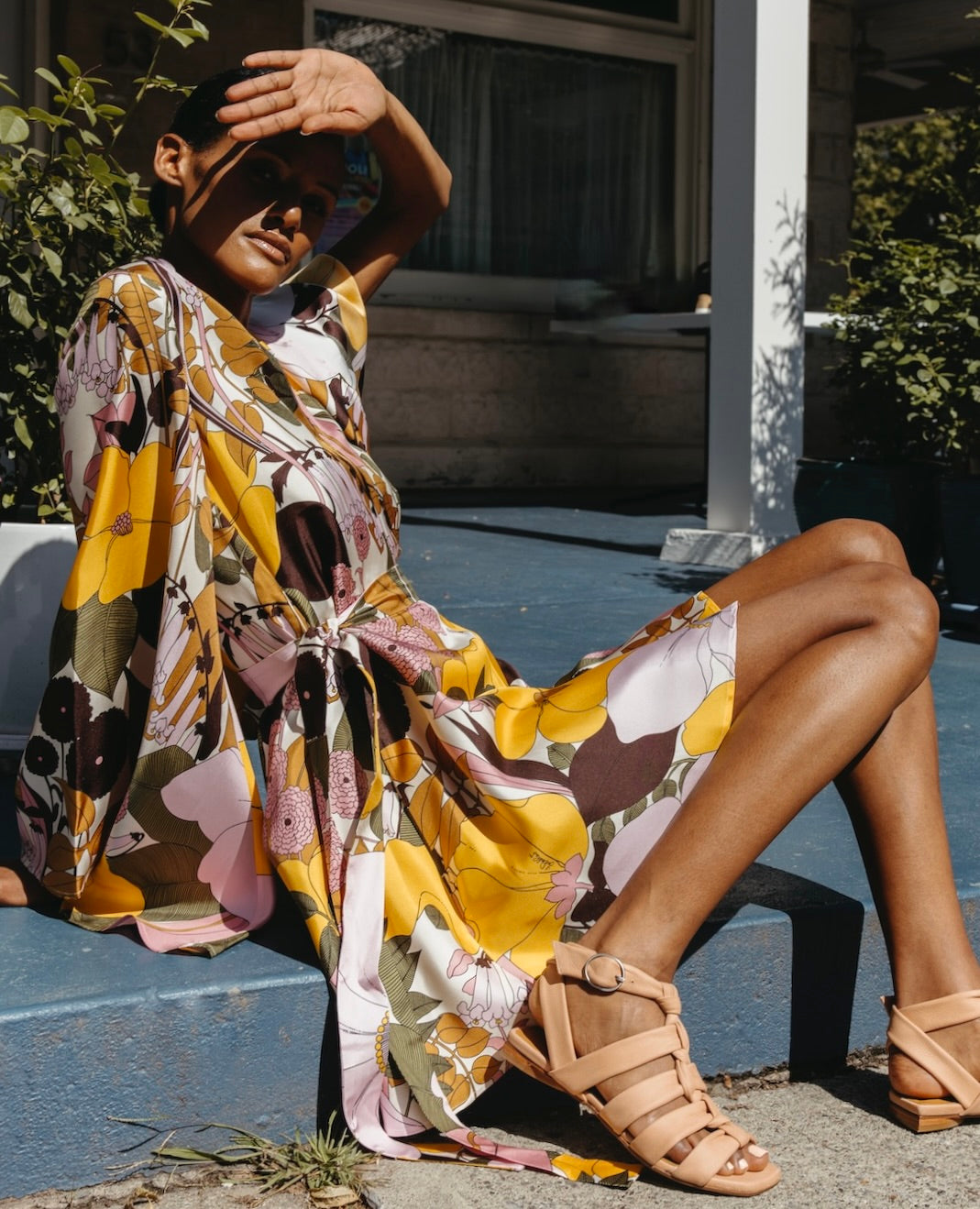 Woman wearing a printed dress and the Flair Sandal in Fawn with her hand blocking her face from the sun. 