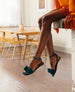 Legs dangling off a counter and feet pictured in the Frances Sandal in Azure with a yellow table and chairs out of focus in the background.  4