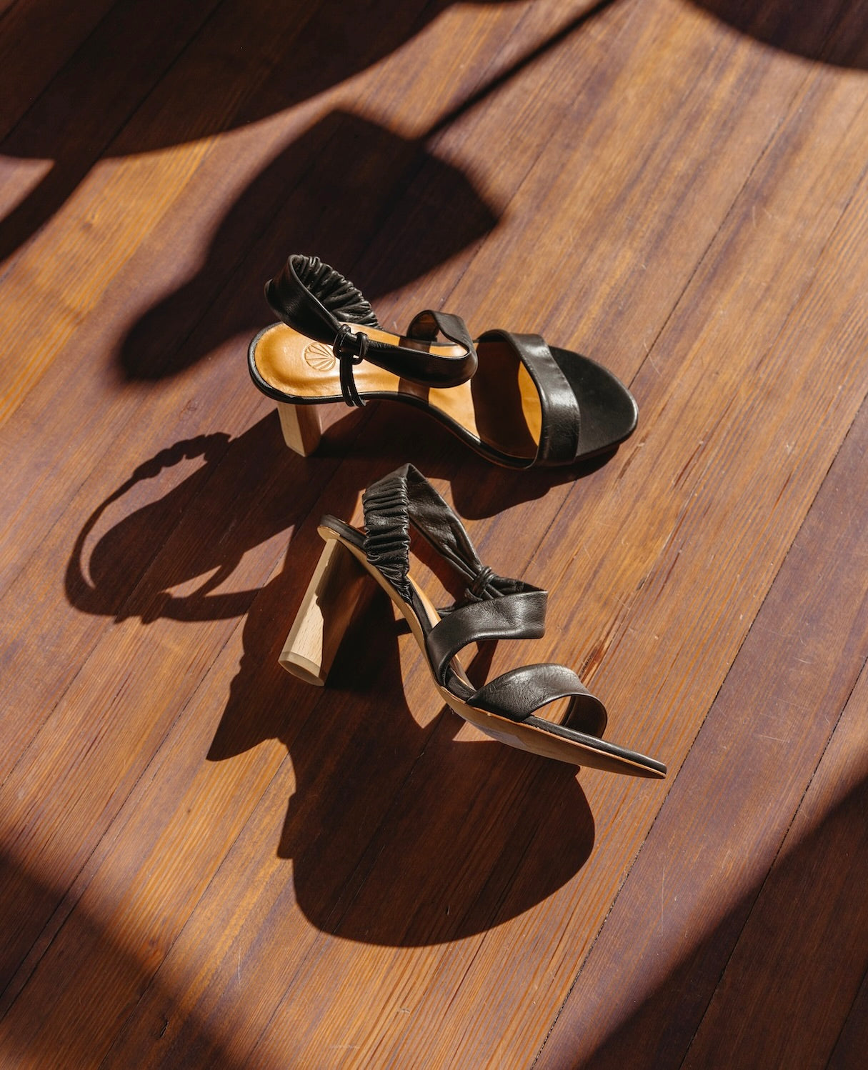 The Gabby Heel in Deep Sea placed on a wooden floor with sunlight beaming and the right heel placed on its side.