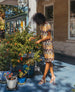 Woman standing outside touching plants and wearing a printed shift dress with the Gabby Heel in Latte Macchiato.  11