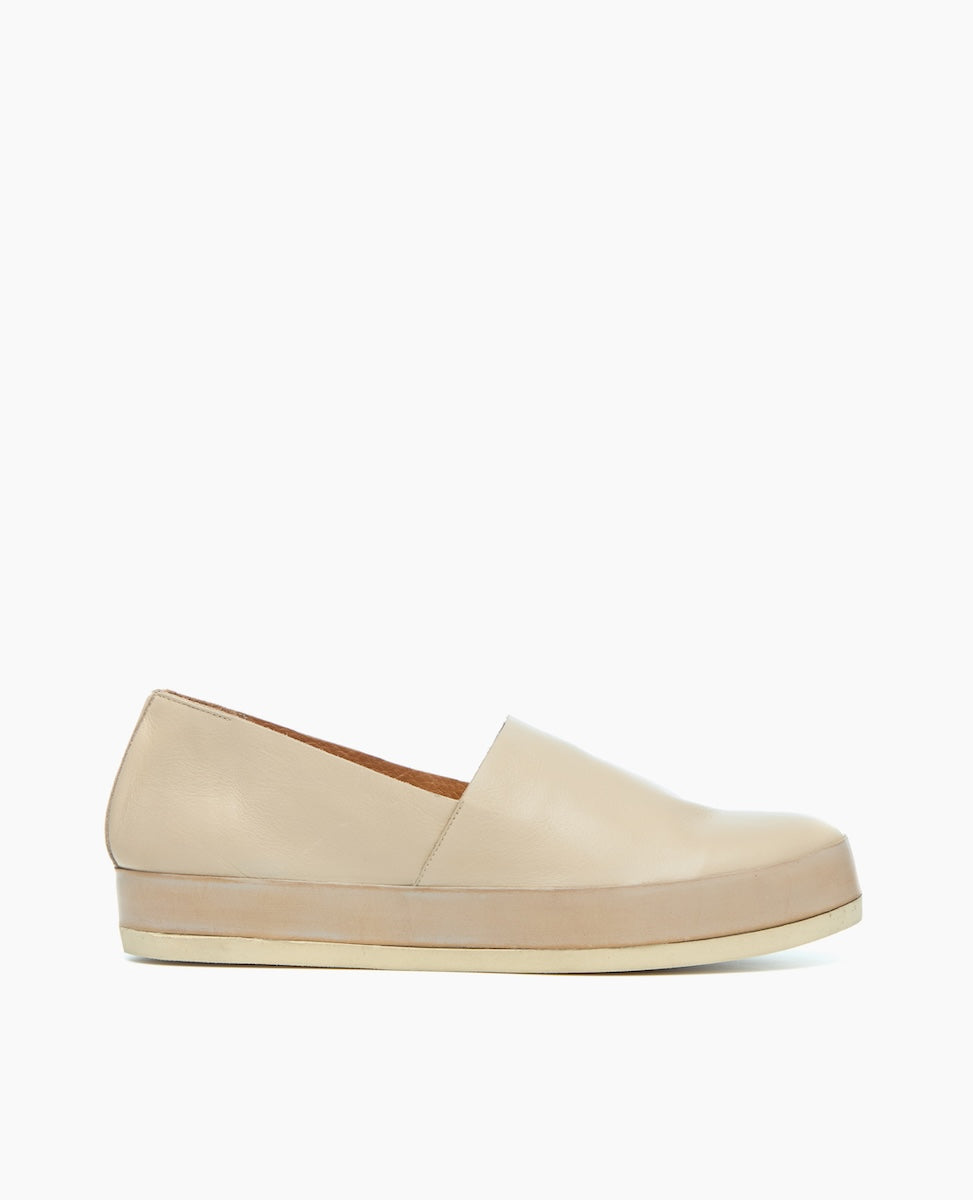 A beige slip-on shoe with a smooth leather upper, a slightly pointed toe, and a flat, light-colored rubber sole.
