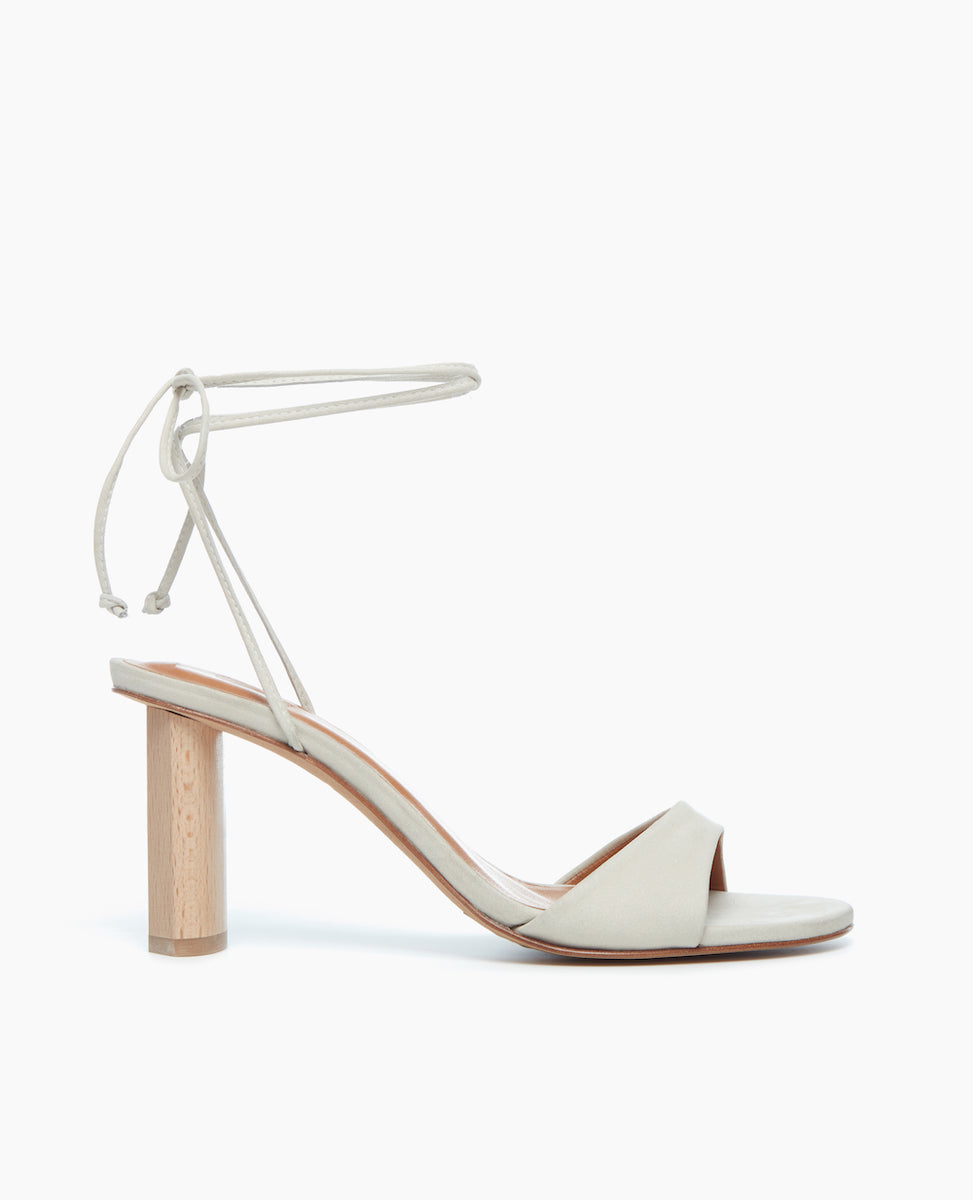 Side view of the Gilda Heel in Griege Nubuck with dainty leather straps that cascade up the ankle finishing in a tie closure. 