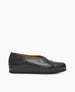 A sleek black leather slip-on shoe with a smooth texture, rounded toe, and a thick, flat sole. 2