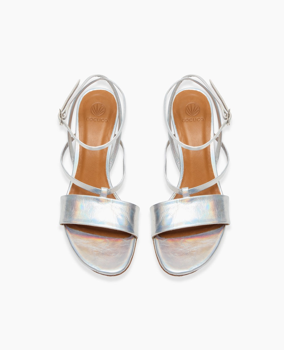 Silver strappy sandals with a shiny, iridescent finish, featuring a tan insole, thin ankle straps, and a small buckle closure.
