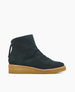 A dark green suede ankle boot with a smooth texture, featuring a rounded toe, a back zipper with a pull tab, and a contrasting tan wedge sole. 4