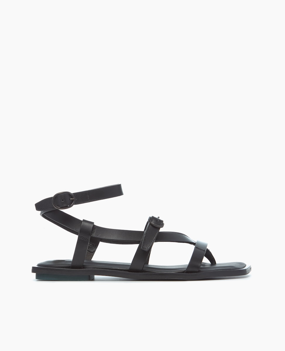 A sleek black sandal featuring a flat sole, multiple thin leather straps crossing over the foot, an adjustable ankle strap with a buckle, and a minimalist design.