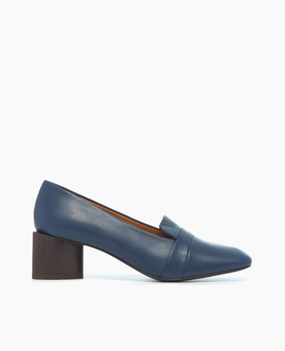 A sleek, blue leather loafer with a pointed toe, a wide strap across the front, and a chunky, dark brown block heel.