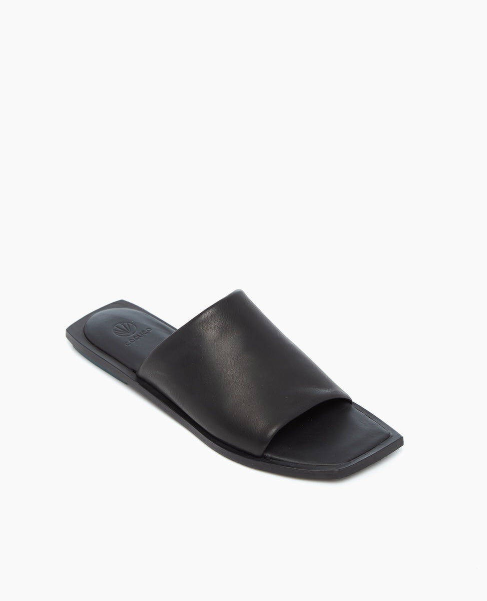 A sleek black slide sandal features a wide, smooth leather strap over the foot, a flat square toe, and a minimalist design with a subtle logo embossed on the insole.