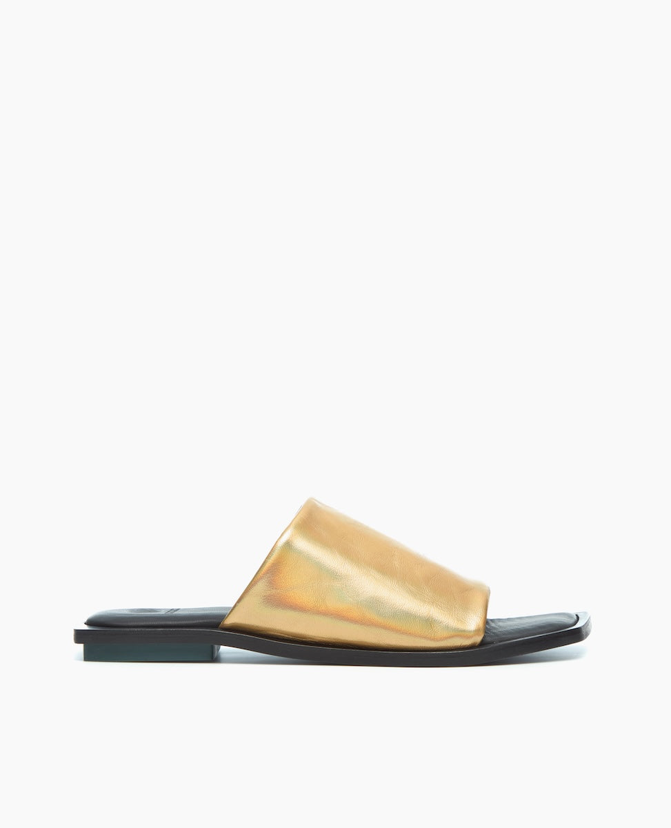 A sleek, flat sandal featuring a shiny gold metallic upper with a wide strap and a contrasting black sole.