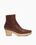 A brown leather ankle boot with a smooth texture, featuring a rounded toe and a light wooden block heel. 4