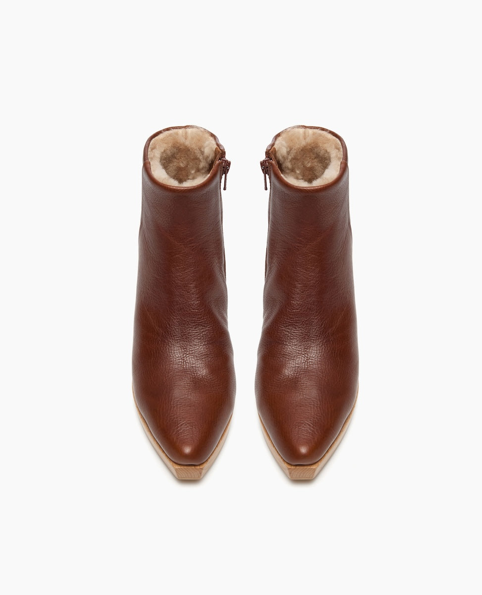 Brown leather ankle boots with a pointed toe, featuring a plush, fur-lined interior and side zippers, showcasing a smooth texture and a sleek, modern design.